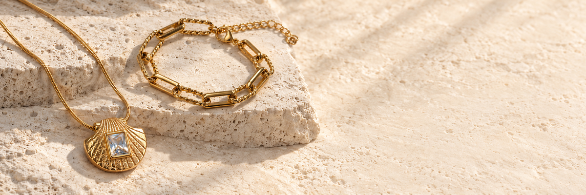 Editorial styling of the Sea Nymphs Shorelight bracelet and Sunlit Scallop necklace on pale stone.