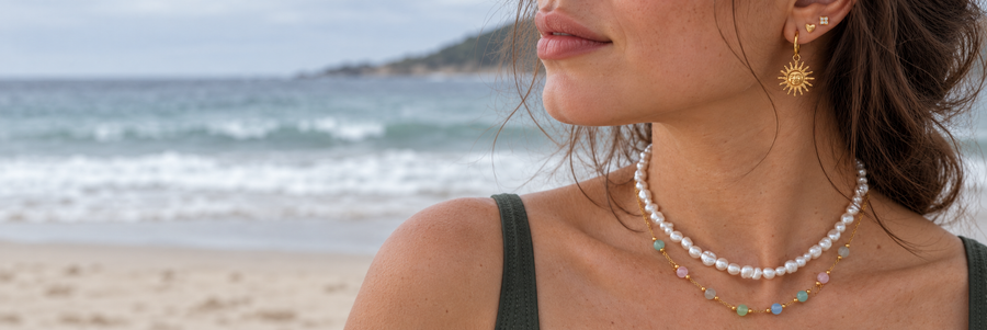 Sea Nymphs three-earring stack and two layered necklaces in a natural beachside portrait.