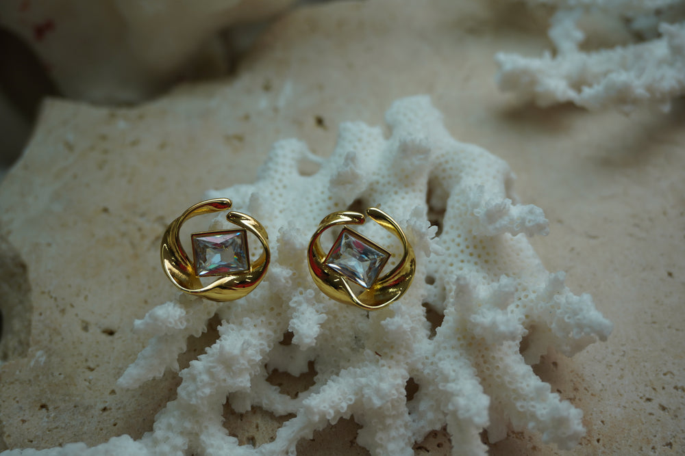 Gold-tone stud earrings with clear square centres framed by flowing open circular curves.