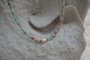 Pale blue beaded necklace with mottled markings, gold-tone spacers and a larger white oval centre bead.