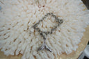 Silver-tone chain bracelet with a textured mermaid-tail charm, pale drop and ring-and-bar fastening.