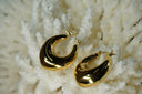 Alternate view: gold-tone broad crescent hoop earrings with smooth reflective surfaces.