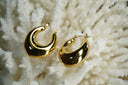 Gold-tone broad crescent hoop earrings with smooth reflective surfaces.