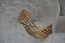 Alternate view: gold-tone open cuff with parallel curved rails crossed by a diagonal centre rail.
