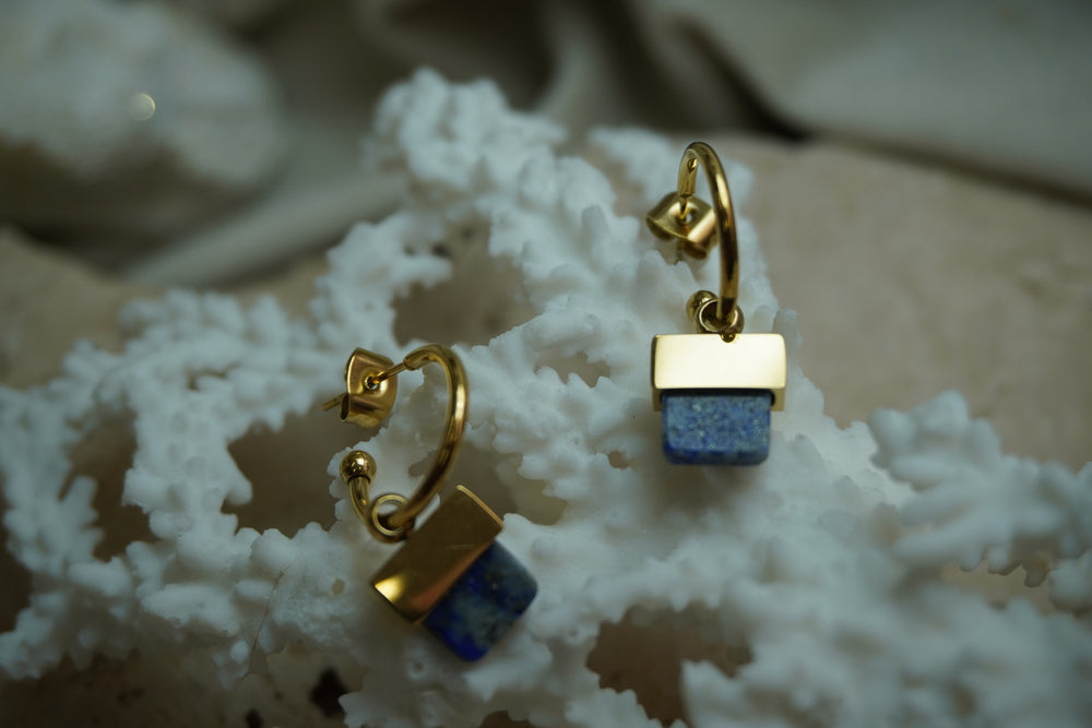 Gold-tone open hoop earrings with rounded ends and mottled blue square drops.