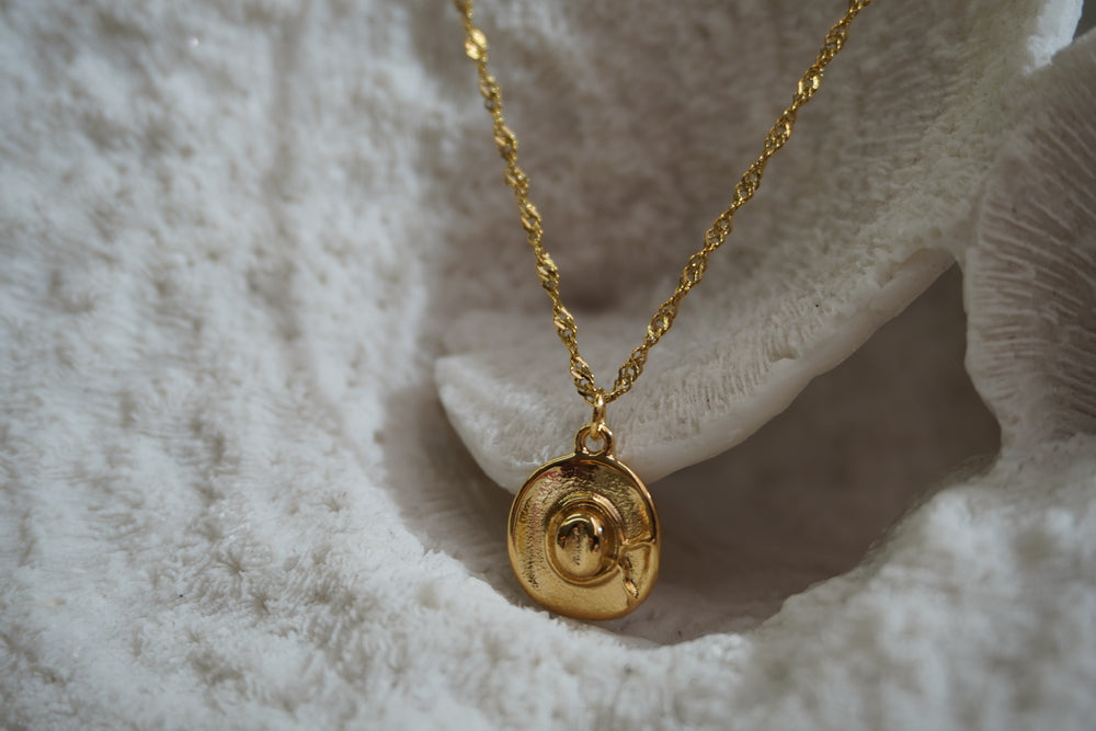 Gold-tone necklace with a western hat pendant, curved brim, bow detail and twisting chain.