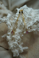 Long gold-tone chain earrings with dark round stud tops, pink faceted teardrops and white oval beads.