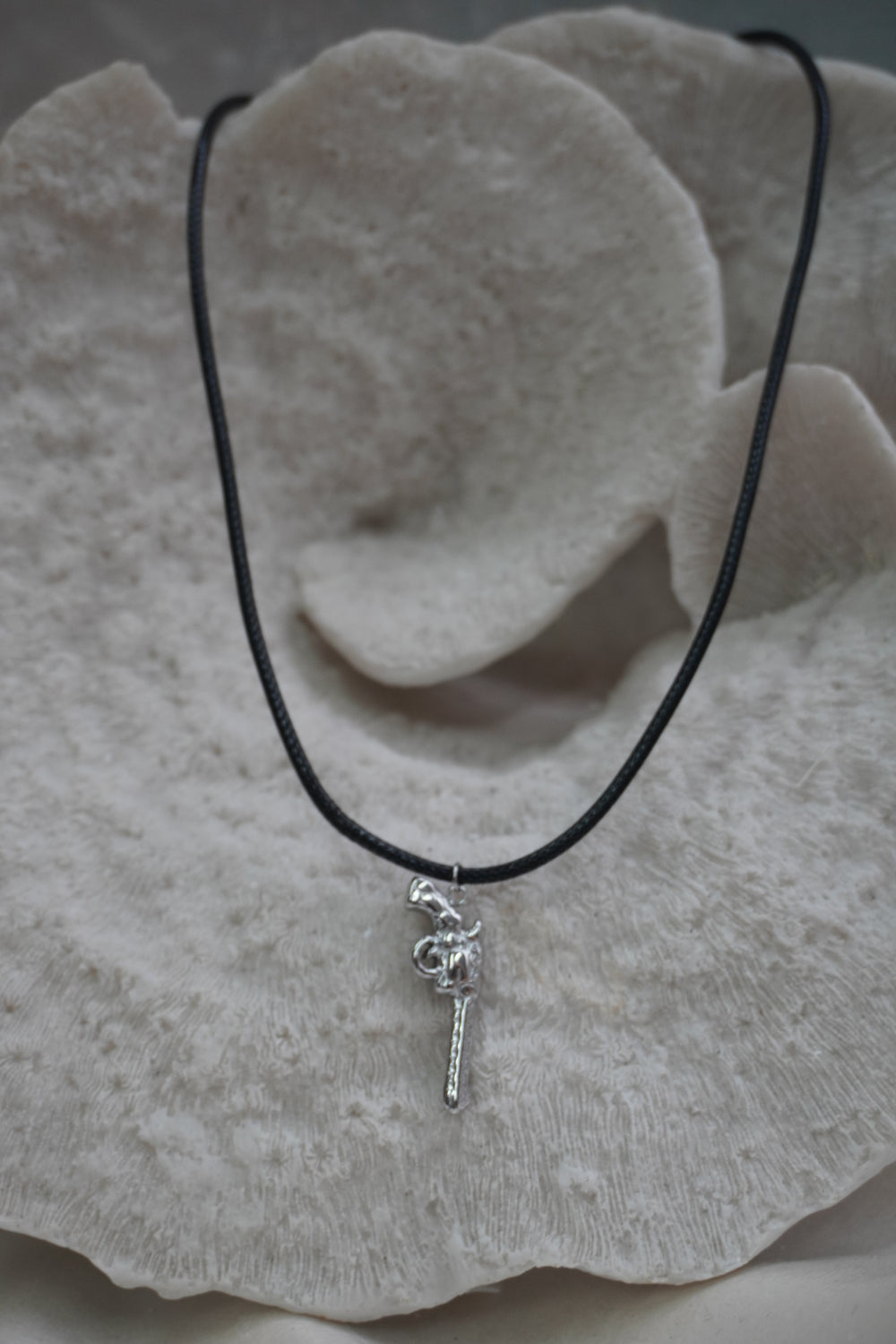 Alternate view: silver-tone revolver-shaped pendant with patterned edges on a black necklace cord.