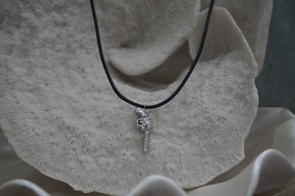 Silver-tone revolver-shaped pendant with patterned edges on a black necklace cord.
