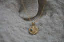 Gold-tone necklace with a textured circular pendant, blue-centred sun and small clear accents.