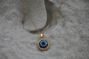 Gold-tone necklace with a blue-and-white eye disc pendant bordered by clear round accents.
