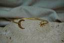Alternate view: gold-tone open cuff with a dimpled crescent moon and a sun with spiral centre and curved rays.