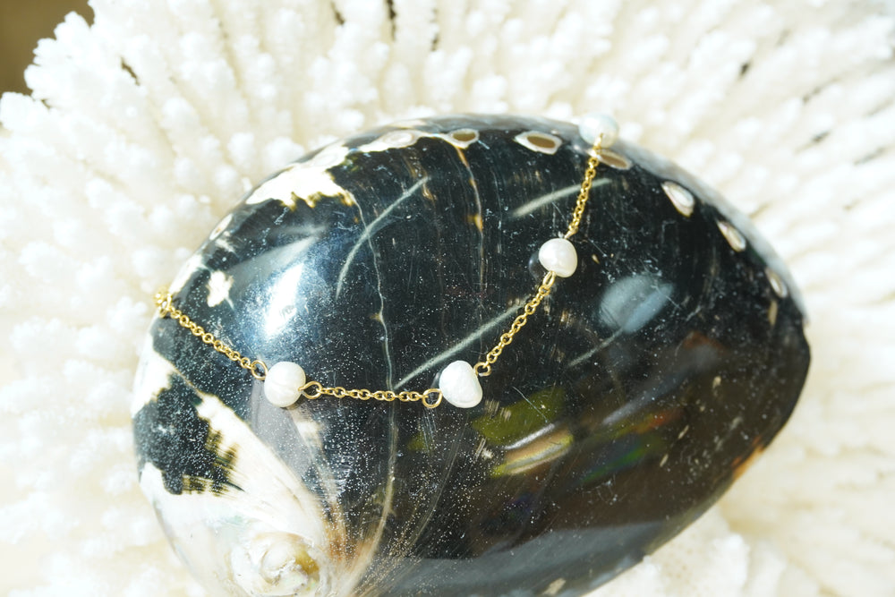 Gold-tone fine chain bracelet with spaced irregular white beads.