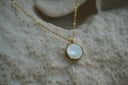 Alternate view: gold-tone chain necklace with a pale reflective circular pendant.