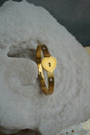 Gold-tone bangle with a heart-shaped centre and dark keyhole detail.
