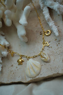 Alternate view: gold-tone long-link necklace with a pale fan-shell shape, a smaller spiral-shell shape, turtle and open sun charms.