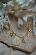Gold-tone long-link necklace with a pale fan-shell shape, a smaller spiral-shell shape, turtle and open sun charms.