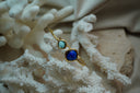 Gold-tone open cuff with a small aqua and a larger deep-blue rounded square faceted accent.