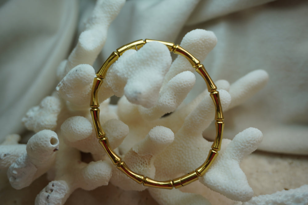Gold-tone bangle with rounded segmented sections and a bamboo-inspired pattern.