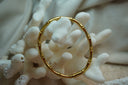 Gold-tone bangle with rounded segmented sections and a bamboo-inspired pattern.