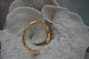 Gold-tone open cuff with an uneven rippled surface and rounded ends.
