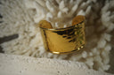 Broad open gold-tone cuff with a dimpled, reflective surface.