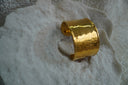 Broad open gold-tone cuff with a dimpled, reflective surface.
