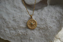 Gold-tone chain necklace with a textured circular pendant, compass-star motif and dark centre.