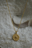 Gold-tone chain necklace with a textured circular pendant, compass-star motif and dark centre.
