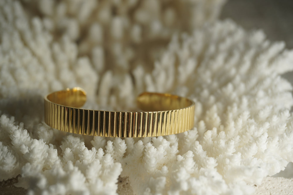 Gold-tone open cuff with closely spaced vertical ridges across a flat band.