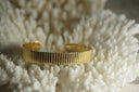 Gold-tone open cuff with closely spaced vertical ridges across a flat band.