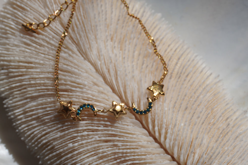 Gold-tone fine-chain bracelet with stars and blue-accented crescent moons.