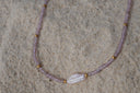 Detail view: lilac faceted-bead necklace with gold-tone spacers and an elongated irregular white centre bead.