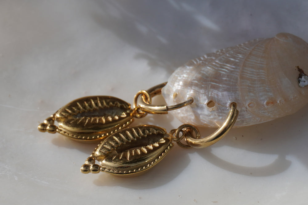 Gold-tone hoop earrings with cowrie-shaped hanging charms, ridged openings and dotted borders.