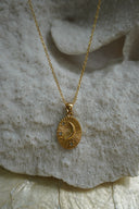 Gold-tone oval pendant necklace with a raised crescent moon, radiating lines and clear accents.