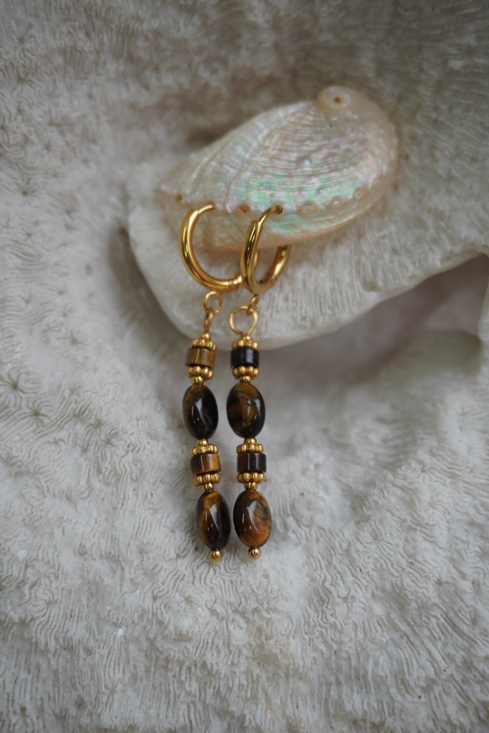 Gold-tone hoop earrings with long drops of brown and near-black oval and cylindrical beads.