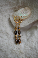 Gold-tone hoop earrings with long drops of brown and near-black oval and cylindrical beads.