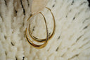 Alternate view: gold-tone elongated open teardrop hoop earrings with tapered upper wires and broader lower curves.