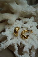 Rounded open gold-tone hoop earrings with an uneven surface and clear accents in diamond-shaped surrounds.