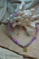 Purple, pink and blue bead necklace with gold-tone spacers and an arched palm-tree and wave charm.