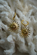 Gold-tone hoop earrings with hanging sun-face charms and pointed rays.