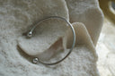 Silver-tone open cuff with a smooth rounded band and spherical end caps.