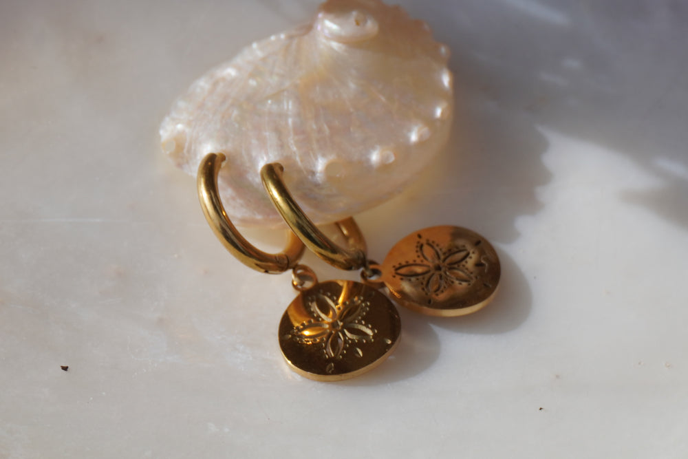 Gold-tone hoop earrings with circular hanging discs and five-petal sand-dollar motifs.