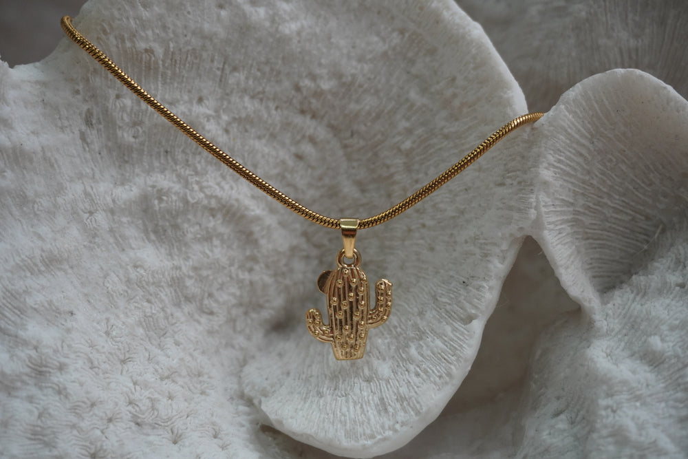 Gold-tone necklace with a ridged, dotted cactus pendant on a close-linked chain.