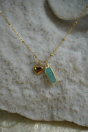 Gold-tone necklace with a blue-green elongated charm and a small heart charm.