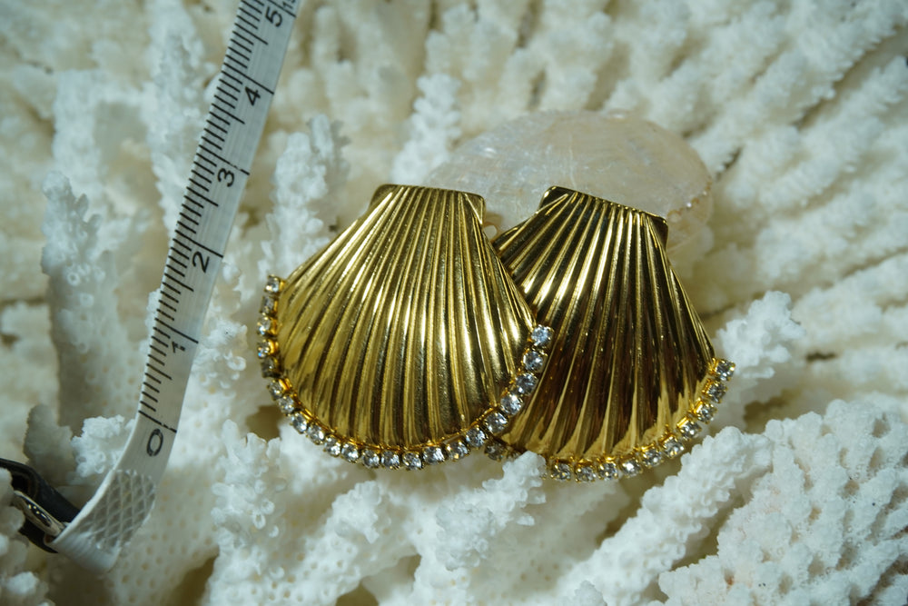 Gold-tone scallop-shell stud earrings with radiating ridges and clear accents along the curved edge.