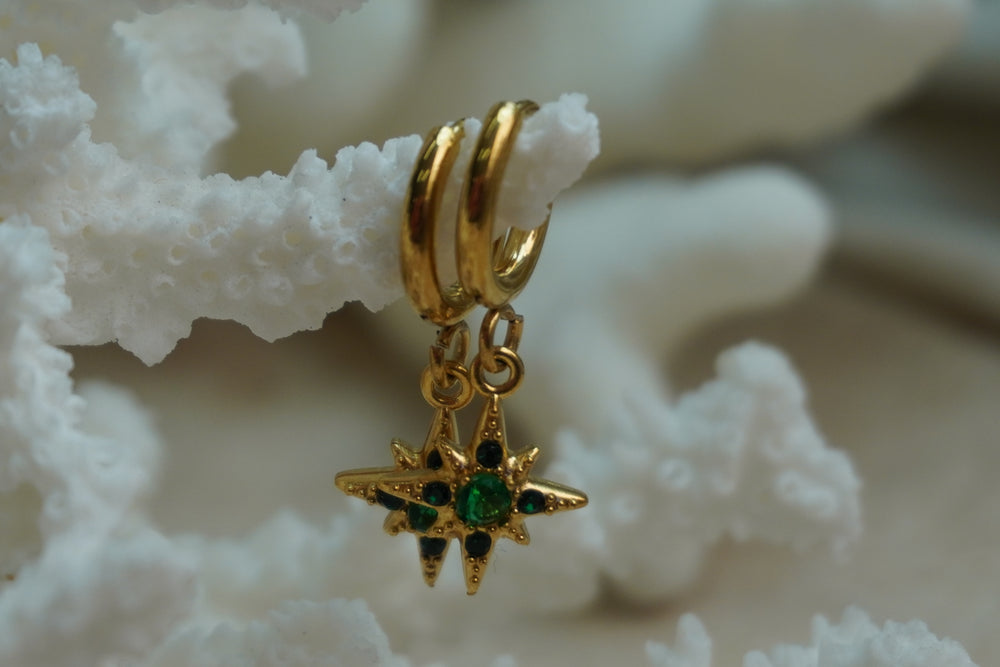 Gold-tone hoops with pointed compass-star charms and green accents.