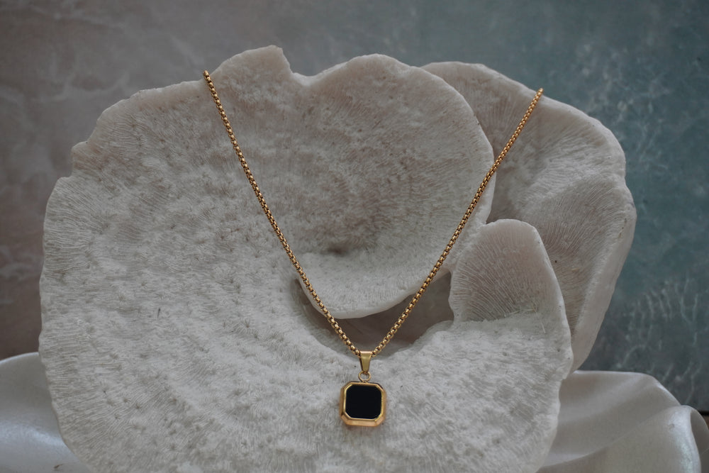 Gold-tone chain necklace with a black square pendant, clipped corners and a smooth border.