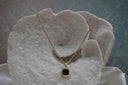 Gold-tone chain necklace with a black square pendant, clipped corners and a smooth border.