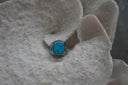 Silver-tone ring with a rounded rectangular blue centre, dark markings, circular blue side accents and patterned borders.